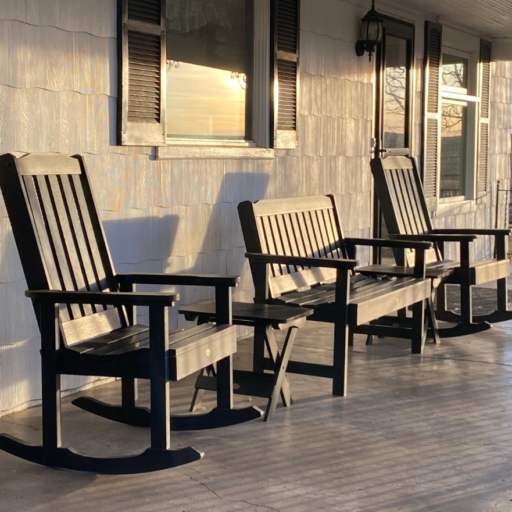 A photo of a front porch with a black bench, with two black rocking chairs on either side. 